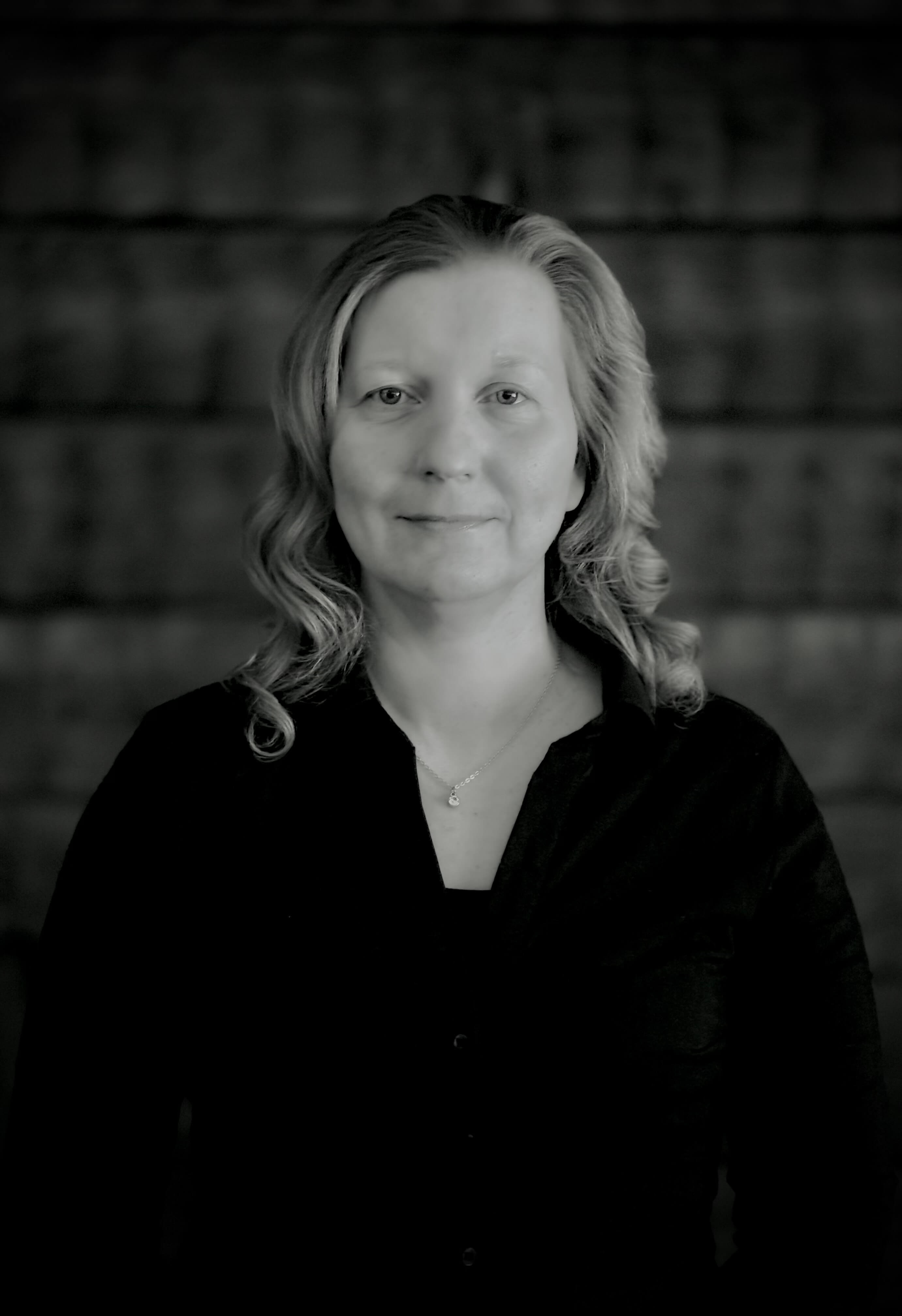 Muotokuva vaaleahiuksisesta naisesta, jolla on musta paita ja hopeinen kaulakoru, harmaasävyinen kuva.